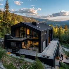 a black house on top of a hill surrounded by trees and mountains in the background