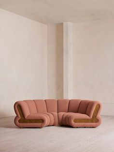 a pink couch sitting on top of a wooden floor next to a white wall in an empty room