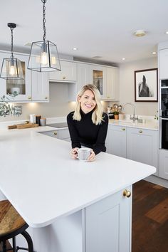 a woman sitting at a kitchen island with a coffee cup in her hand and smiling