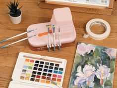 there are some art supplies on the table with it's paintbrushes and watercolors