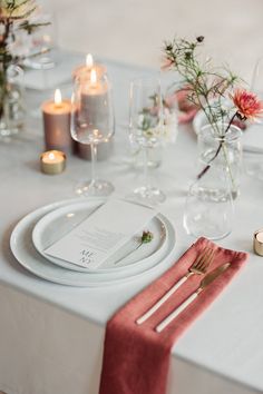 the table is set with white plates, silverware and pink napkins on it