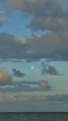 the moon is setting over the ocean with clouds in the sky and on the water