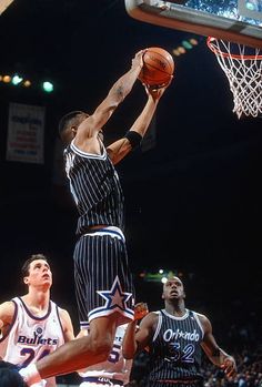 a basketball player dunks the ball in front of two other players during a game