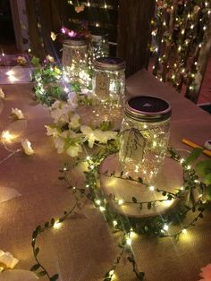 some mason jars are sitting on a table with flowers and fairy lights around the jar