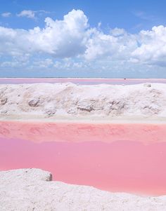 pink water in the middle of a desert with white clouds above it and blue sky