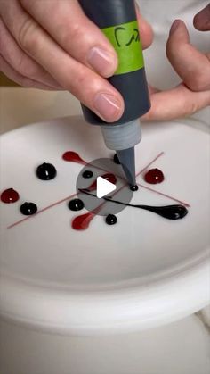 a person is using a marker to paint a piece of art on a white plate