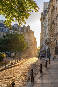 a cobblestone street with people walking on it and buildings in the background at sunset