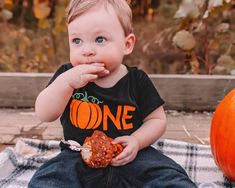 a little boy sitting on the ground eating something out of his hand while wearing a black shirt