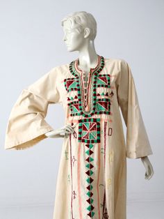 "This is a vintage long tunic or kurta. Intricate embroidery details the front of the cream canvas dress with green and burgundy tones. It features belled sleeves and a knotted button up front. CONDITION In good condition with wear consistent with age and use. There is some light browning on the back shoulder and sleeves. MEASUREMENTS Bust: 40\" ... 101.6 cm Hips: 52\" ... 132.1 cm Length: 56\" ... 142.2 cm Shoulders: 13.5\" ... 34.3 cm Sleeves: 15.5\" ... 39.4 cm Neck to Sleeve End: 32\" ... 81 Bohemian Kaftan With Embroidered Long Sleeves, Fall Bohemian Embroidered Cotton Dress, Bohemian Cotton Long Sleeve Thobe, Bohemian Long Sleeve Embroidered Cotton Dress, Bohemian Cotton Thobe With Long Sleeves, Green Bohemian Kaftan With Intricate Embroidery, Traditional Long Sleeve Tunic With Embroidered Sleeves, Bohemian Beige Embroidered Dress With Intricate Details, Bohemian Long Sleeve Thobe For Spring