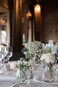 two vases with flowers are sitting on a table in front of empty wine glasses