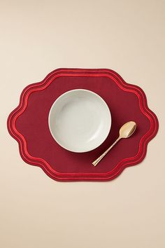 a red place mat with a white bowl and spoon on it next to a fork