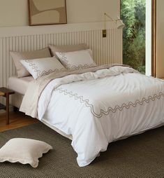 a white bed sitting in a bedroom next to a wooden dresser and window on top of a hard wood floor