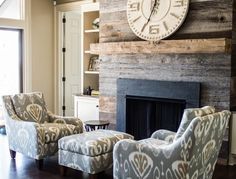 a living room with two chairs and a large clock on the wall above it's fireplace