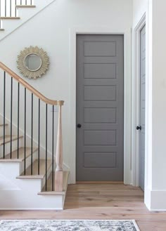 a gray door in a white room with stairs and rugs on the wooden floor