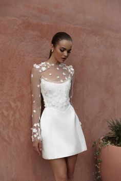 a woman in a short white dress standing next to a wall with flowers on it