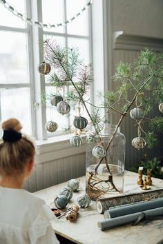 a woman sitting at a table in front of a christmas tree with ornaments hanging from it