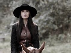 a woman wearing a hat riding on the back of a brown horse in a field