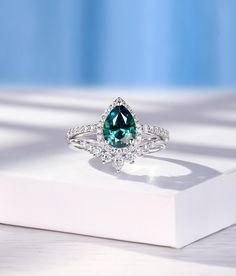 a ring with a large green stone surrounded by diamonds on top of a white box