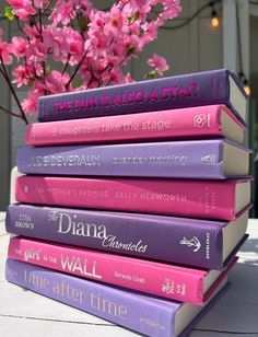 a stack of books sitting on top of a table next to a vase with pink flowers