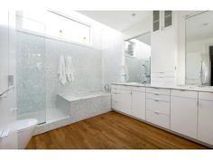 a white bathroom with wooden floors and cabinets in the shower area, along with a large mirror