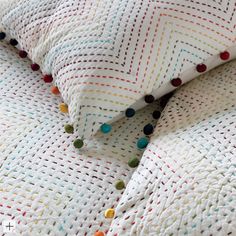 a close up of a bed with white and multi colored pillows on it's side