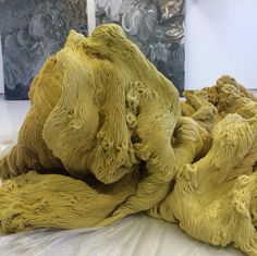 a pile of yellow yarn on top of a white table cloth next to two paintings