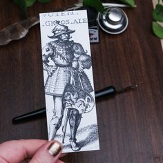 a person holding up a bookmark with an image of a man wearing a hat