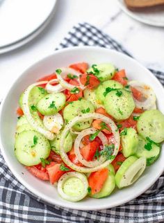 a white bowl filled with cucumber and tomatoes on top of a checkered table cloth