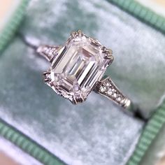 an emerald colored diamond ring sitting on top of a green velvet covered cushioned box