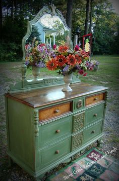 a green dresser with flowers on top and a mirror in the back, sitting outside