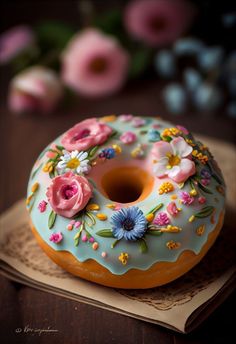 a frosted donut with flowers on it sitting on top of a table next to a book