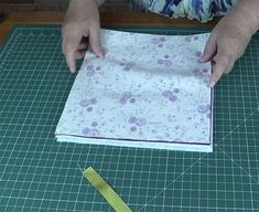 a person cutting fabric with scissors on top of a green mat and some yellow tape