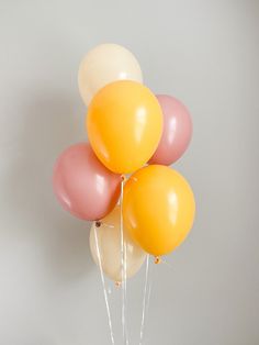 a bunch of balloons floating in the air on top of a white table with pink and yellow ribbons