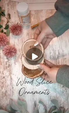 two hands are holding a wooden slice ornament on a table with pink flowers