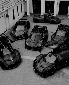 black and white photograph of five supercars parked in front of a house on the street