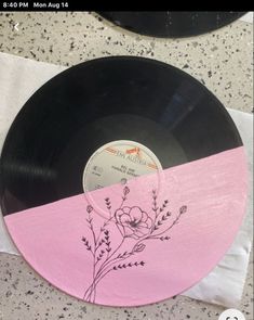 a pink and black vinyl record on a table with a white napkin around it that has a flower drawn on the side