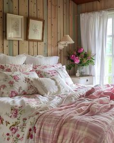 a bed with pink and white comforter in a bedroom next to a window filled with flowers