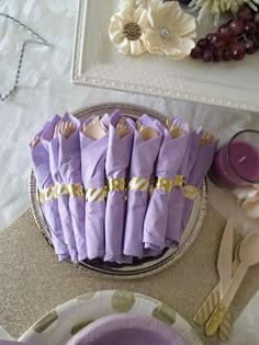 purple napkins with gold trim are sitting on a silver platter next to flowers and candles