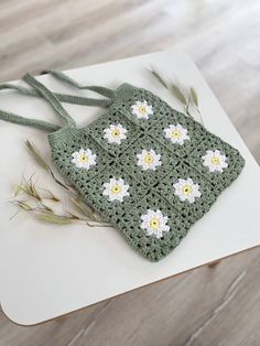 a green crocheted bag with white and yellow flowers on it sitting on top of a table