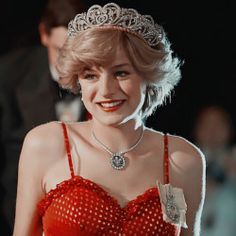 a woman in a red dress wearing a tiara and smiling at the camera while standing next to other people