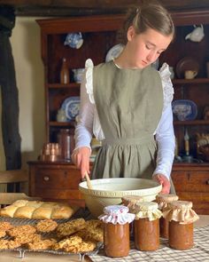 a woman in an apron is making some food on a table with cookies and other pastries