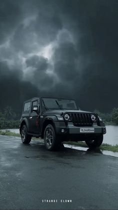 a black jeep parked on the side of a road in front of a dark cloudy sky