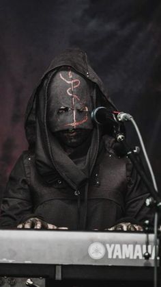 a man with his face painted like a snake and wearing a black hoodie sits at a keyboard