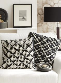 two black and white pillows sitting on top of a white couch next to a lamp