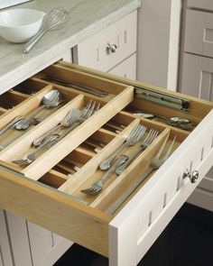 an open drawer in a kitchen with silverware and utensils on the drawers