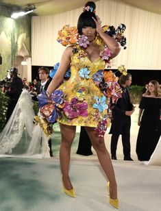 a woman in a yellow dress with flowers on her head and heels standing next to other people