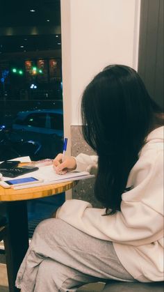 a woman sitting at a table writing on a piece of paper with a pen in her hand