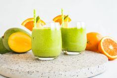 two glasses filled with green smoothie next to oranges