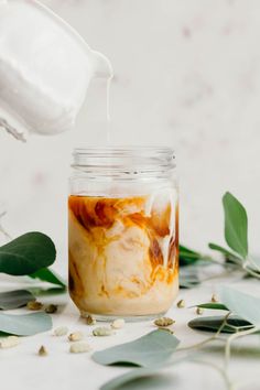 a glass jar filled with food next to green leaves and milk being poured into it