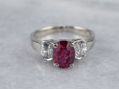 Always in style, rings such as this one can be worn as engagement rings, birthstone rings, or just for special occasions. We've set the center of this one with a high-quality, glowing red ruby. The side stones are bright white diamonds, reflecting plenty of light into the center stone. As an engagement ring will look well with a variety of bands, from a plain golden circle to a ruby and diamond eternity band. Metal: 14K White Gold Gem: Ruby 2.02 Carats Gem Measurements: 8.0 x 6.0 mm, Oval Accents: 8 Diamonds totaling .50 Carats, G in Color, SI1 in Clarity Ring Size: 6.75 Marks: “14K MFP” Stamped on the inside band Classic Three Stone Ruby Ring With Diamonds, Classic Red Three Stone Diamond Ring, Red Three-stone Diamond Ring For Anniversary, Red Three-stone Diamond Promise Ring, Fine Jewelry Red Diamond Three Stone Ring, Red Three Stone Diamond Ring For Promise, Red Three Stone Diamond Promise Ring, Classic Three Stone Ruby Ring, Classic Three-stone Ruby Ring